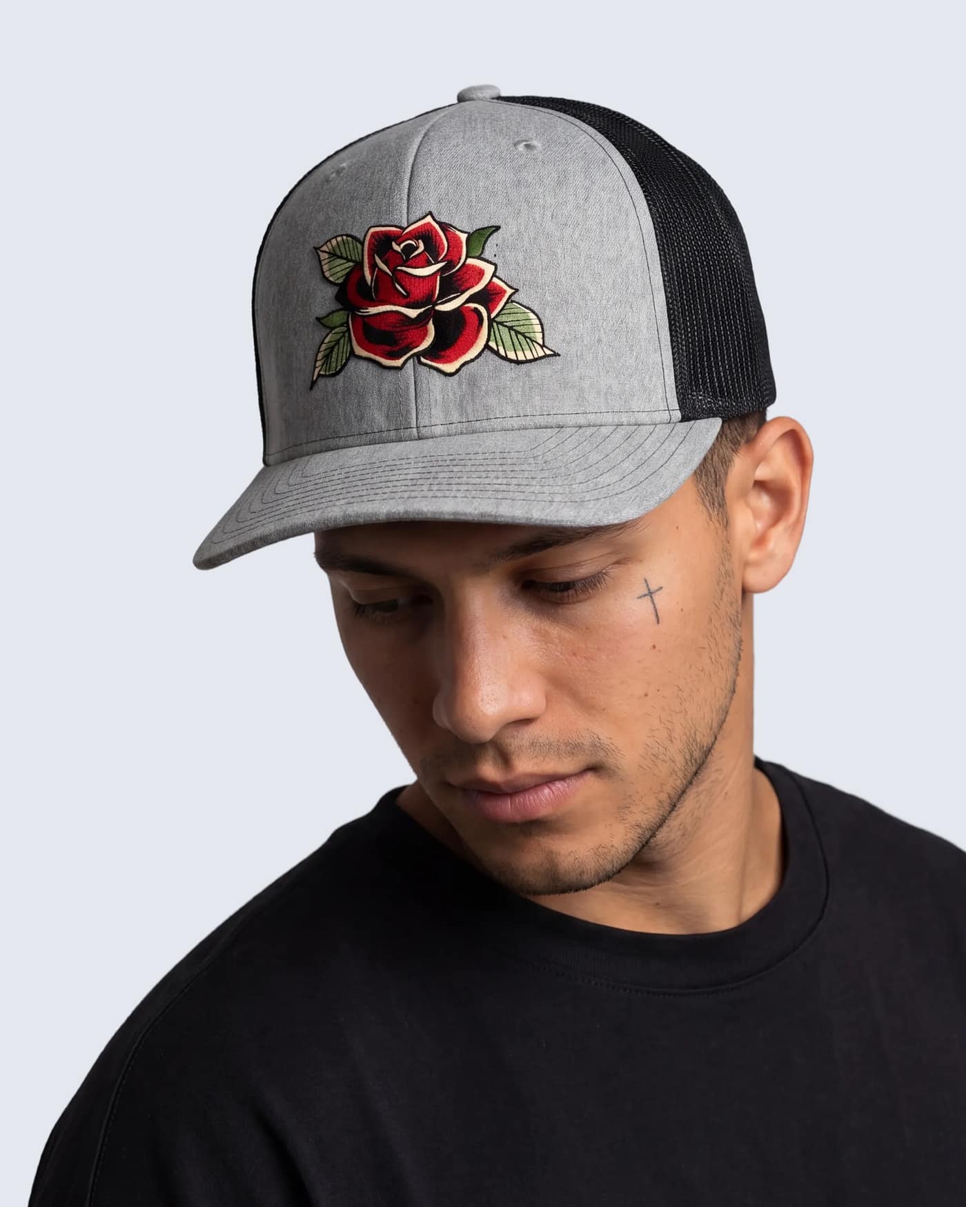 FERN + FIN RESISTENCIA TRUCHA gray and black trucker cap with embroidered red rose graphic shown in front profile on model wearing black shirt.