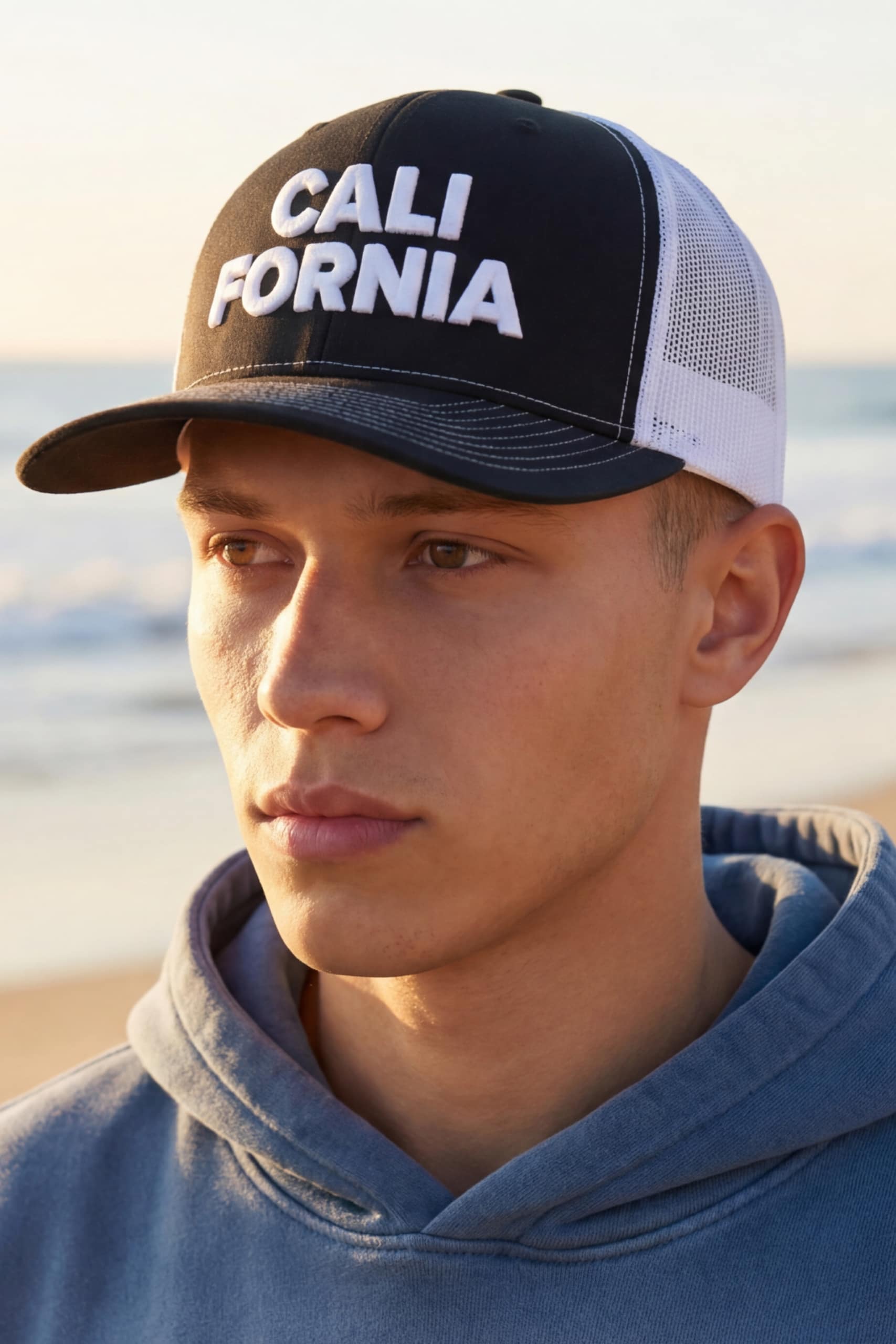Black and white California trucker hat worn by male model at beach during sunset