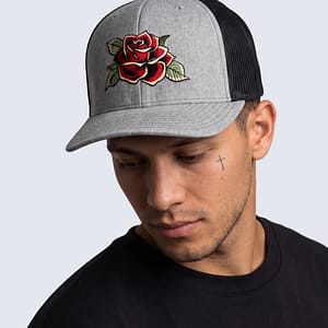 FERN + FIN RESISTENCIA TRUCHA gray and black trucker cap with embroidered red rose graphic shown in front profile on model wearing black shirt.