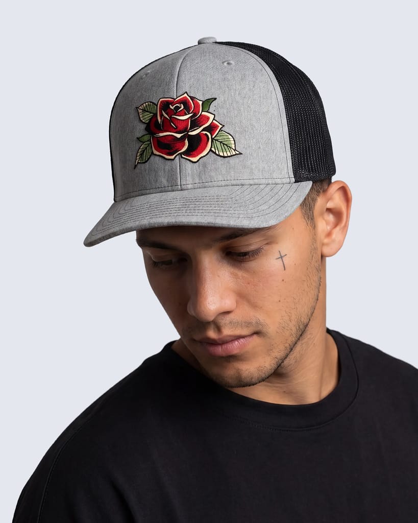 FERN + FIN RESISTENCIA TRUCHA gray and black trucker cap with embroidered red rose graphic shown in front profile on model wearing black shirt.