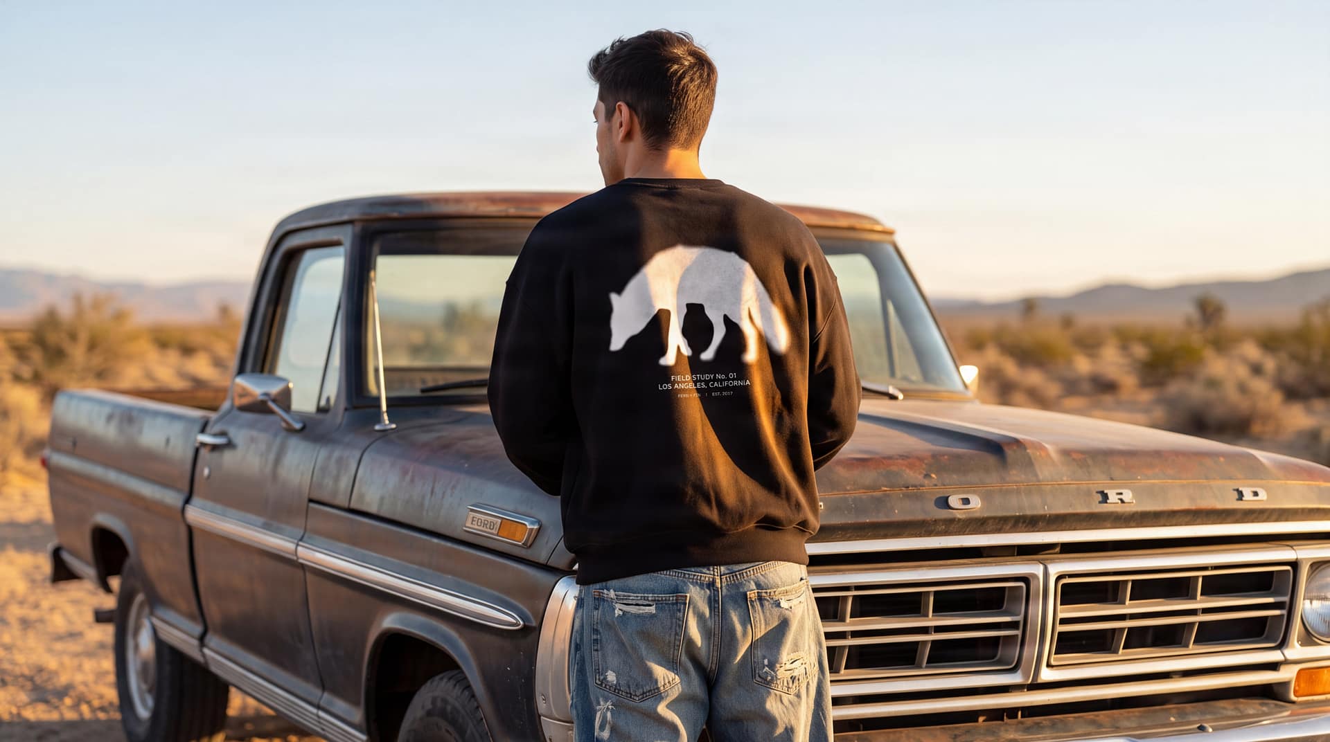 Model wearing the FERN + FIN Field Study No. 01 sweatshirt beside a vintage truck in warm desert light.